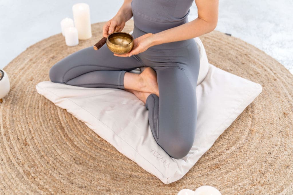 Eine Frau meditiert mit einer Klangschale auf einem Meditationsset von Vedara